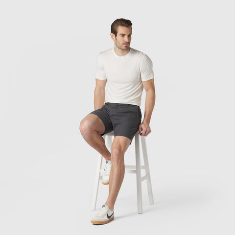 Man wearing Jetsetter Tech Short in gray, seated on a white stool against a minimal backdrop.