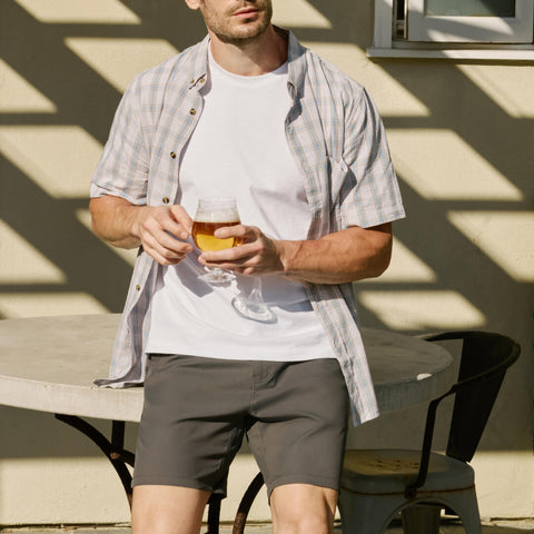 Man wearing Jetsetter Tech Short with a casual shirt outdoors drinking a beverage.