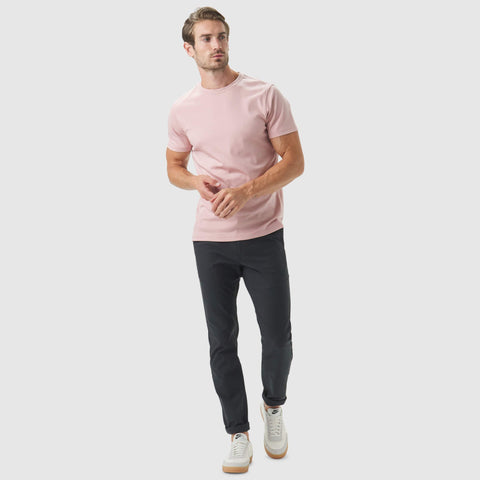 Man wearing Jetsetter Tech Pant Slim Fit with pink shirt and white sneakers, showcasing a stylish and comfortable look.