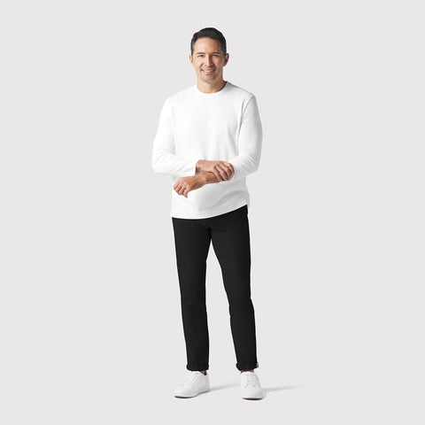 Man wearing Jetsetter Tech Pant Slim Fit in black with white sneakers and a white sweater.