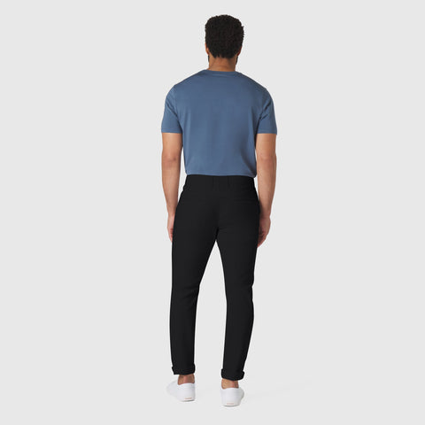 Man wearing slim fit Jetsetter Tech Pant in black, showcasing wrinkle-free, anti-odor, and shape-retention features for travel-friendly use.