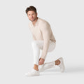 Man wearing Legacy Polo Sweater in beige, squatting with white pants and shoes.