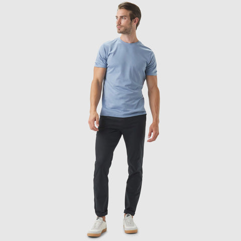 Man wearing Jetsetter Tech Pant Slim Fit with a light blue t-shirt, showcasing wrinkle-free, anti-odor, stain-repellent pants.