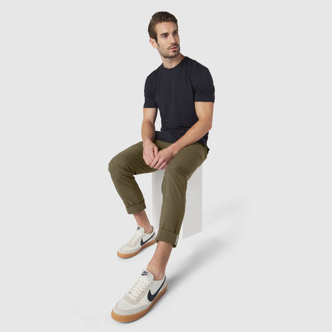 Man wearing Jetsetter Tech Pant Slim Fit in olive green, sitting casually with reflective detailing on cuff.